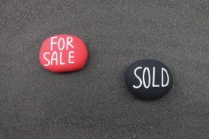 For Sale, Sold text carved on stones over black volcanic sand