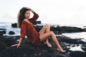 Young slender female model sitting on rock at ocean coast